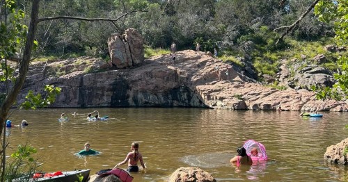 Devil’s Waterhole in Texas, with crystal-clear green water inviting swimmers beneath pink granite cliffs.