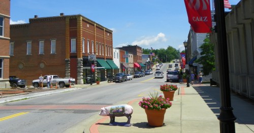 View of downtown Cadiz, Kentucky, on a summer day with a little pig statue in the foreground and historic brick buildings lining the street.