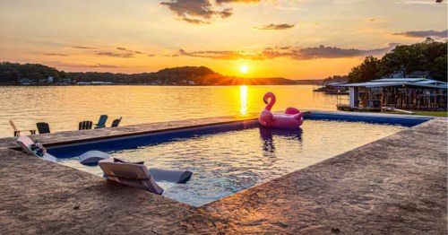 In-ground pool with a pink flamingo float facing a gorgeous lake sunset at a Missouri Airbnb.