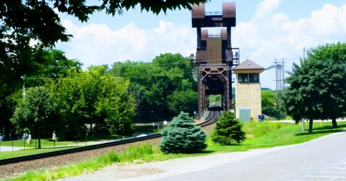 Railroad tracks leading toward a historic lift bridge in a green Wisconsin park