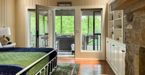 interior of a pangburn arkansas bedroom with built-ins, a stone fireplace, and doors to a porch with a hot tub overlooking the river