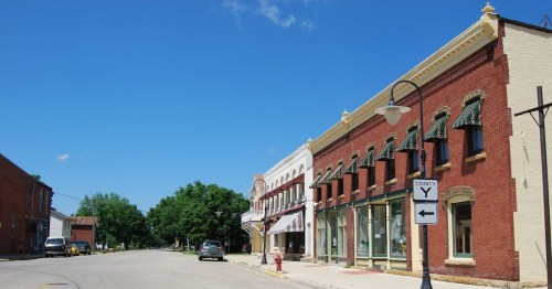 Historic brick storefronts with green awnings along a sunny street corner in Mazomanie, Wisconsin.
