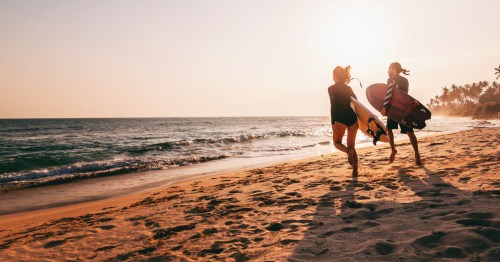 A couple runs across a sandy beach toward the ocean while holding surfboards in California.