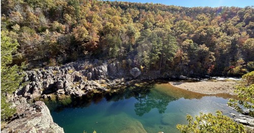 High-angle view of a clear green river pool surrounded by autumn trees in Missouri.