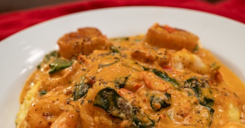 Close up of a white bowl with homemade shrimp and grits with veggies and a sauce