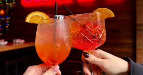 Two hands toasting with a pair of spritzes at Happy Camper in Chicago, Illinois.