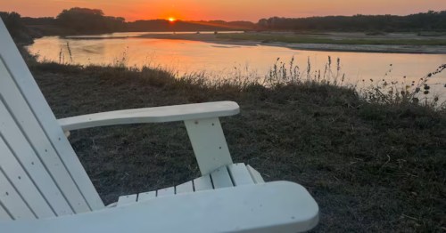 White Adirondack chair facing a stunning river sunset at a Dannebrog, NE Airbnb.