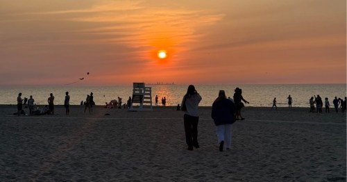 Silhouetted beachgoers watching a vibrant orange sunset over Lake Michigan at Chesterton's dunes.