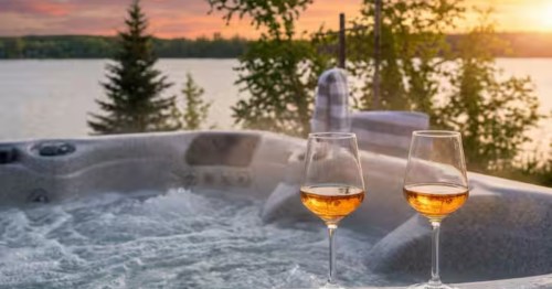 Two wine glasses sitting next to a bubbling hot tub at a waterfront Crosslake, MN Airbnb at sunset.
