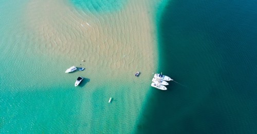 Boats anchored on a shallow turquoise sandbar meeting deep blue water at Torch Lake, Michigan.