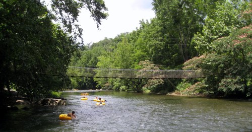 A group of tubers on the Little River near Townsend, Tennessee, on a summer day with a swinging bridge in the background.