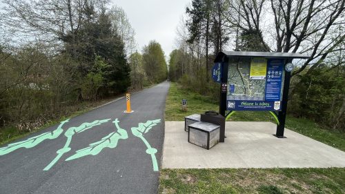 A trail with a map kiosk and green leaf designs on the path, surrounded by trees and greenery.