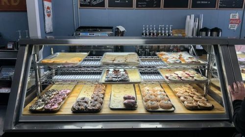 A display case filled with various pastries and donuts, with a menu board in the background.