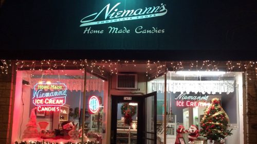 A festive storefront with holiday decorations, featuring "Niemann's Homemade Candies" and a Christmas tree in the window.