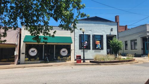 A sunny street scene featuring colorful storefronts, outdoor seating, and a clear blue sky.