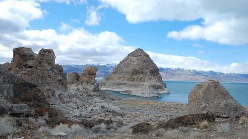 A rocky landscape with unique formations and a large island in a blue lake under a cloudy sky.