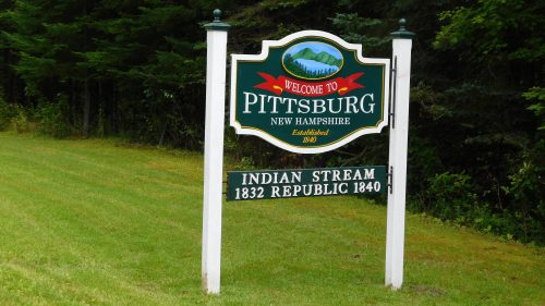 Welcome sign for Pittsburg, New Hampshire, featuring establishment dates and a scenic background.