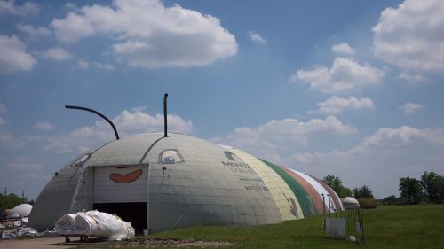 A large, dome-shaped building with a cartoonish face and antennae, set against a blue sky with fluffy clouds.