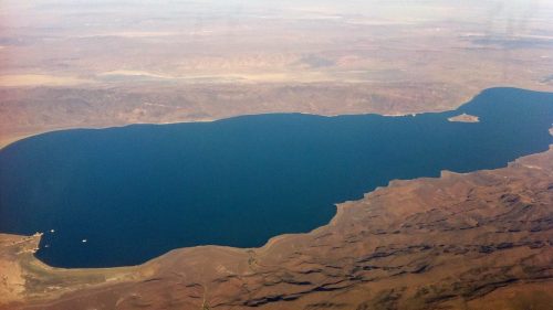 Aerial view of a large blue lake surrounded by arid land and mountains under a clear sky.