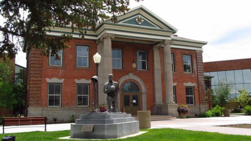Historic brick building with columns, a statue in front, and landscaped green space.