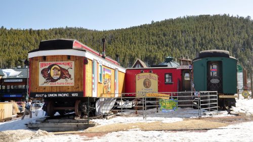Colorful vintage train cars displayed in a snowy area, surrounded by trees and rustic signage.