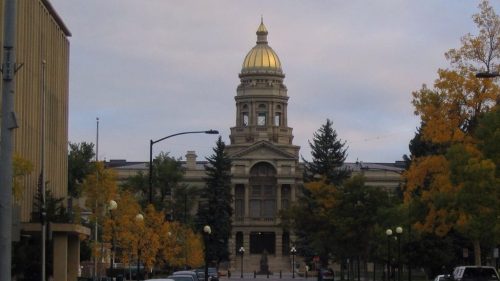 A grand building with a golden dome, surrounded by trees and autumn foliage, along a quiet street.