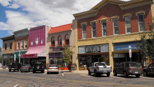 A charming street scene featuring colorful storefronts and parked cars under a partly cloudy sky.