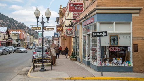 A charming street scene with shops, street signs, and pedestrians in a small town, featuring vintage storefronts and a cloudy sky.