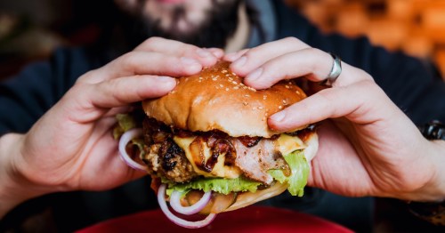 Young man eating a cheeseburger filled with onions, lettuce, and cheese.