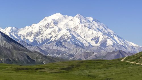 Snow-capped mountain peak rises above green valleys under a clear blue sky.