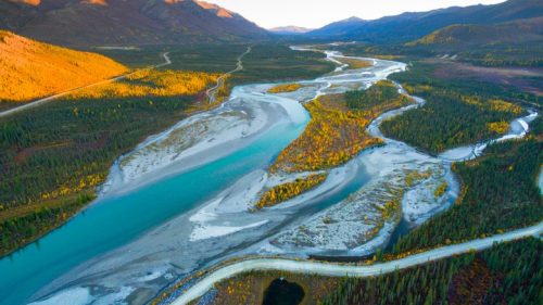Aerial view of a winding river surrounded by colorful autumn foliage and mountains in the background.