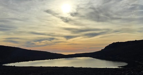 An orange and yellow sunset lights up the sky above a remote lake in Hawaii.