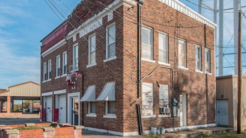 Historic brick building with white trim, striped awnings, and utility lines, set against a clear blue sky.