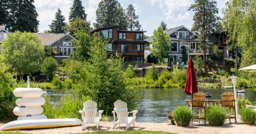 Two chairs sit on the banks of the Deschutes River in Oregon in front of an Airbnb.