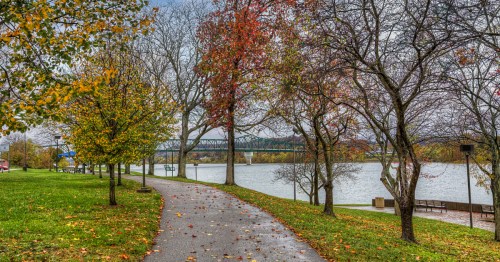 A paved path winds along the Ohio River toward a truss bridge in Huntington, West Virginia, on a rainy autumn day.