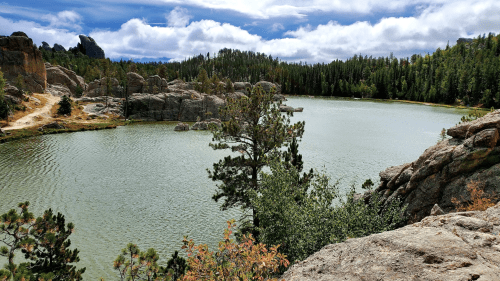 A serene lake surrounded by rocky formations and lush green trees under a cloudy sky.