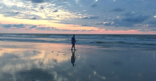 A silhouette walks along a beach in Virginia at sunrise.