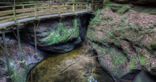 A wooden boardwalk overlooks a pond surrounded by rock walls.