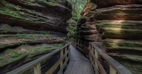 A wooden boardwalk winds between mossy rock walls.