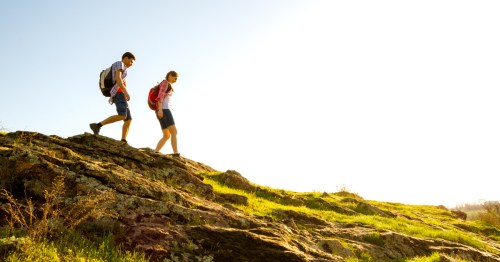 A young couple hikes down a rocky trail on a clear summer day.