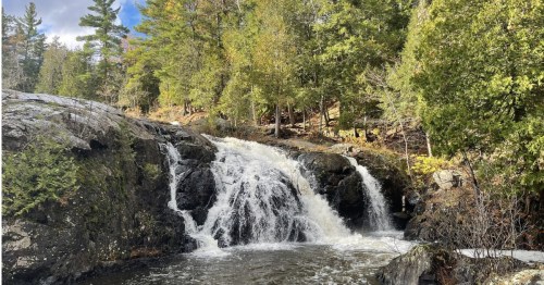Scenic waterfall rushing over dark rocks with early autumn trees at Dead River Falls in Marquette, MI.