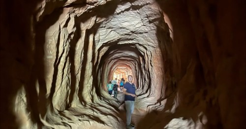 Visitors walking through the Belly of the Dragon tunnel in Utah, surrounded by smooth, carved sandstone walls.
