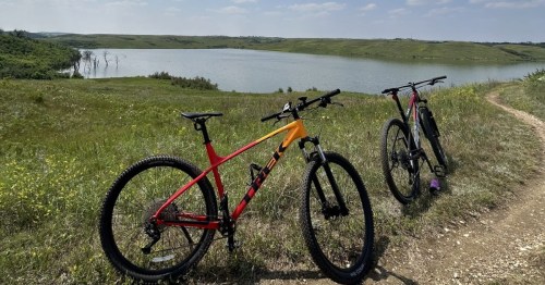 Mountain bikes parked on a grassy trail overlooking scenic Harmon Lake Recreation Area in North Dakota.
