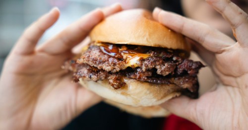 hands holding a burger with double patty, sauce, and cheese