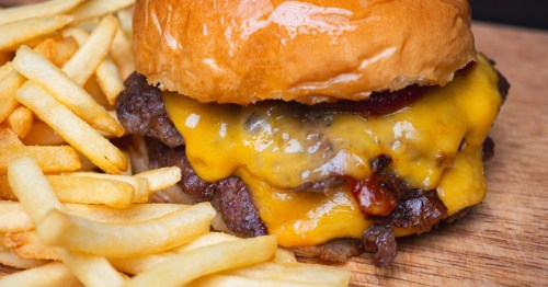 a double cheeseburger and a side of fries on a wood board