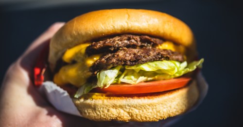 hands holding a double cheeseburger with lettuce and tomato