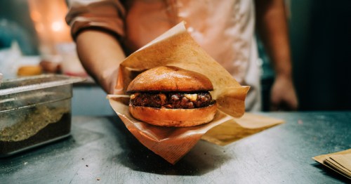 a chef holds out a smashburger wrapped in brown paper