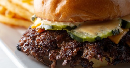 closeup of a smashburger with pickles and sauce on a plate with a side of french fries