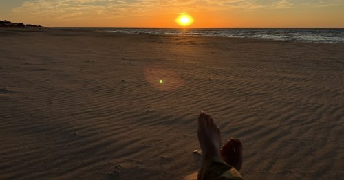 Bare feet on sandy Lake Michigan beach watching a sunset at Nordhouse Dunes, MI.