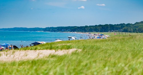 Turquoise lakefront with sandy beach and umbrellas and sunbathers along the coast.